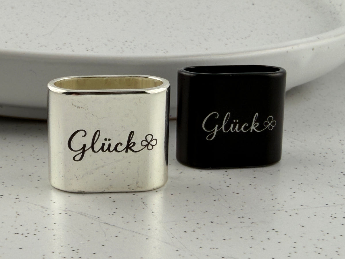 Detailaufnahme eines gravierten Zwischenstücks mit dem Schriftzug "Glück" und einem Kleeblatt